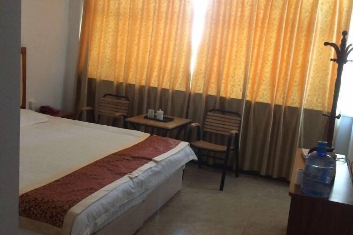 Une chambre d’hôtel comprenant un lit, un bureau, deux chaises, un distributeur d’eau et des rideaux.