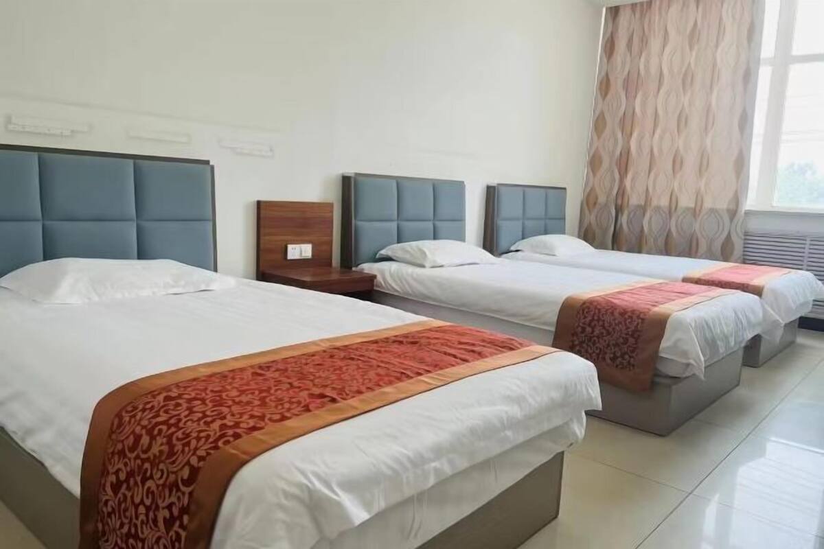Une chambre d’hôtel avec trois lits, chacun doté d’une tête de lit et d’un pied de lit, et une fenêtre avec des rideaux.