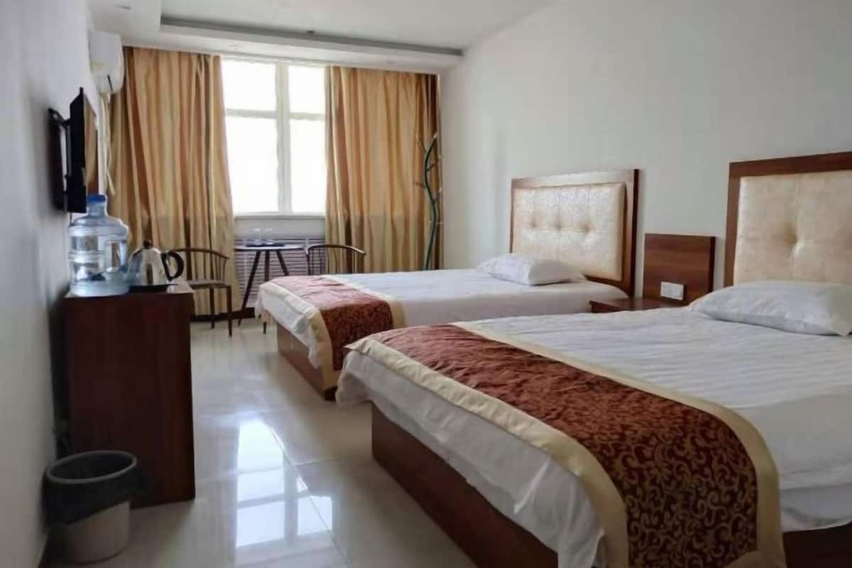 Une chambre d’hôtel avec deux lits, un bureau avec une chaise, un distributeur d’eau et une fenêtre avec des rideaux.