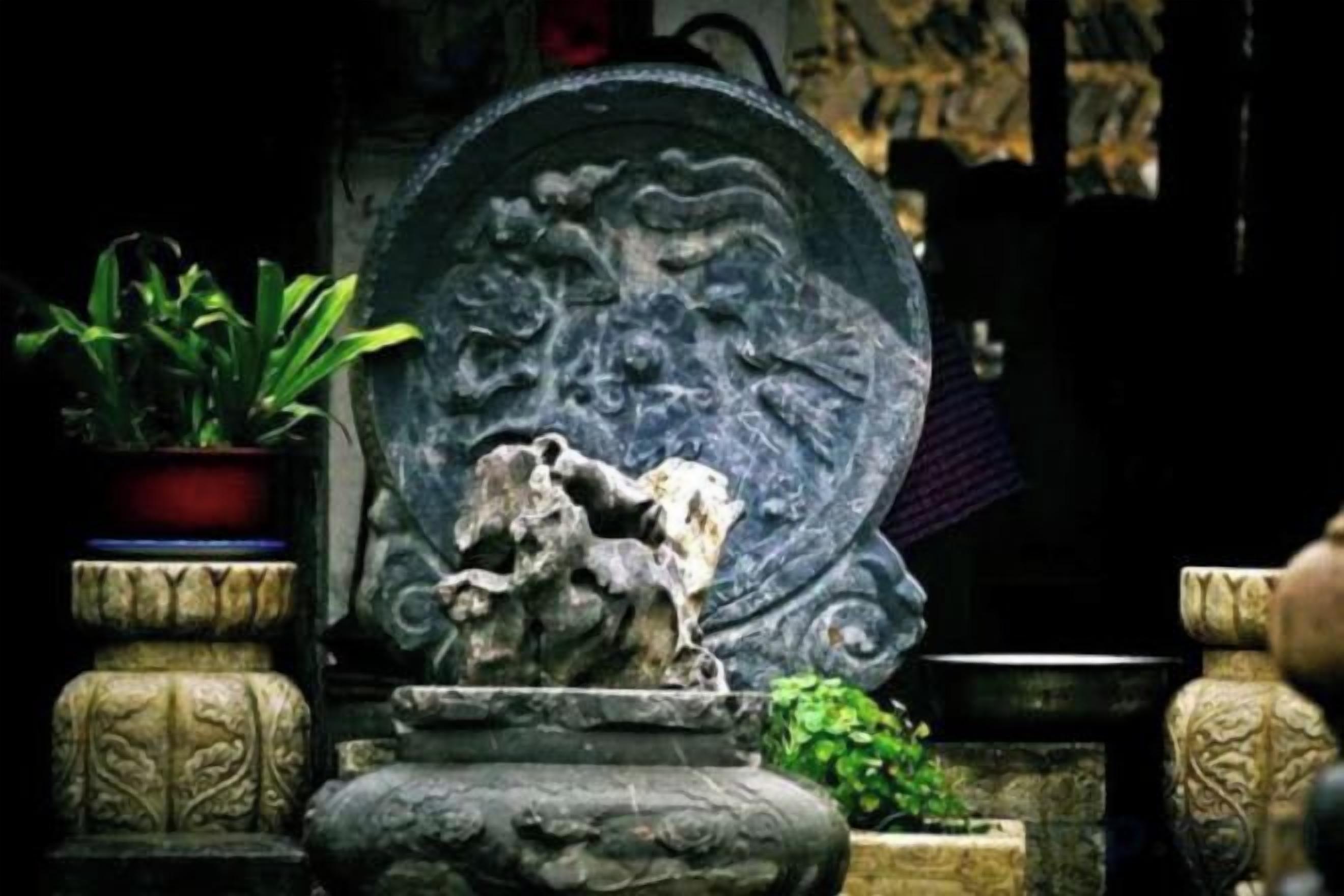 A stone fountain with a horse sculpture, surrounded by potted plants and stone structures.