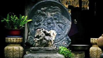 A stone fountain with a horse sculpture, surrounded by potted plants and stone structures.