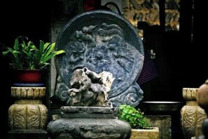 A stone fountain with a horse sculpture, surrounded by potted plants and stone structures. - Tiankeyu Inn, Luxian County (Jing County)