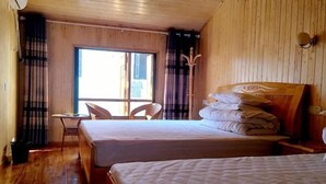Una habitación con dos camas, piso de madera, una ventana y una silla.