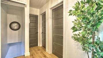 Un couloir avec un plancher en bois, une horloge au mur et une plante en pot.