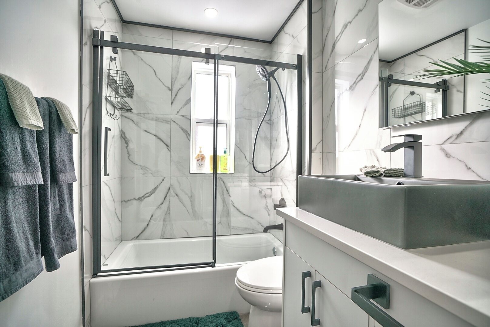 Een moderne badkamer met een douche met glazen wand, een witte badkuip en een wastafelmeubel met wastafel en spiegel.