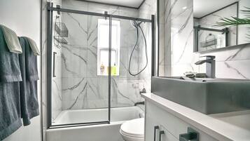 Een moderne badkamer met een douche met glazen wand, een witte badkuip en een wastafelmeubel met wastafel en spiegel.