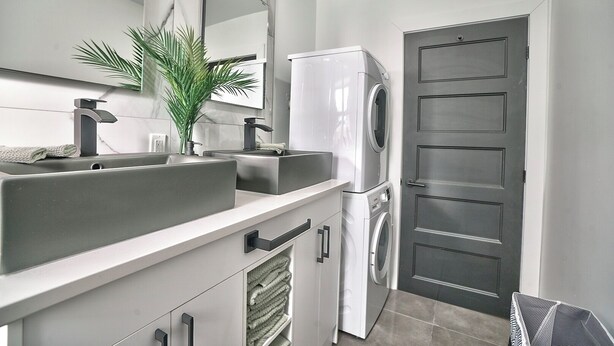 A modern kitchen with a double sink, a built-in washing machine, and a door with a panel design.