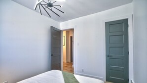 A bedroom with a bed, a green throw, a modern ceiling light, and two doors.