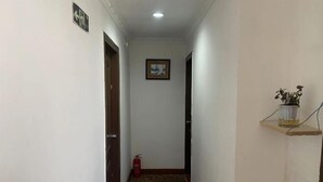 A narrow hallway with patterned carpet, a fire extinguisher, a framed picture on the wall, and a small shelf with a plant. - Jinju Hostel (Shanghai)