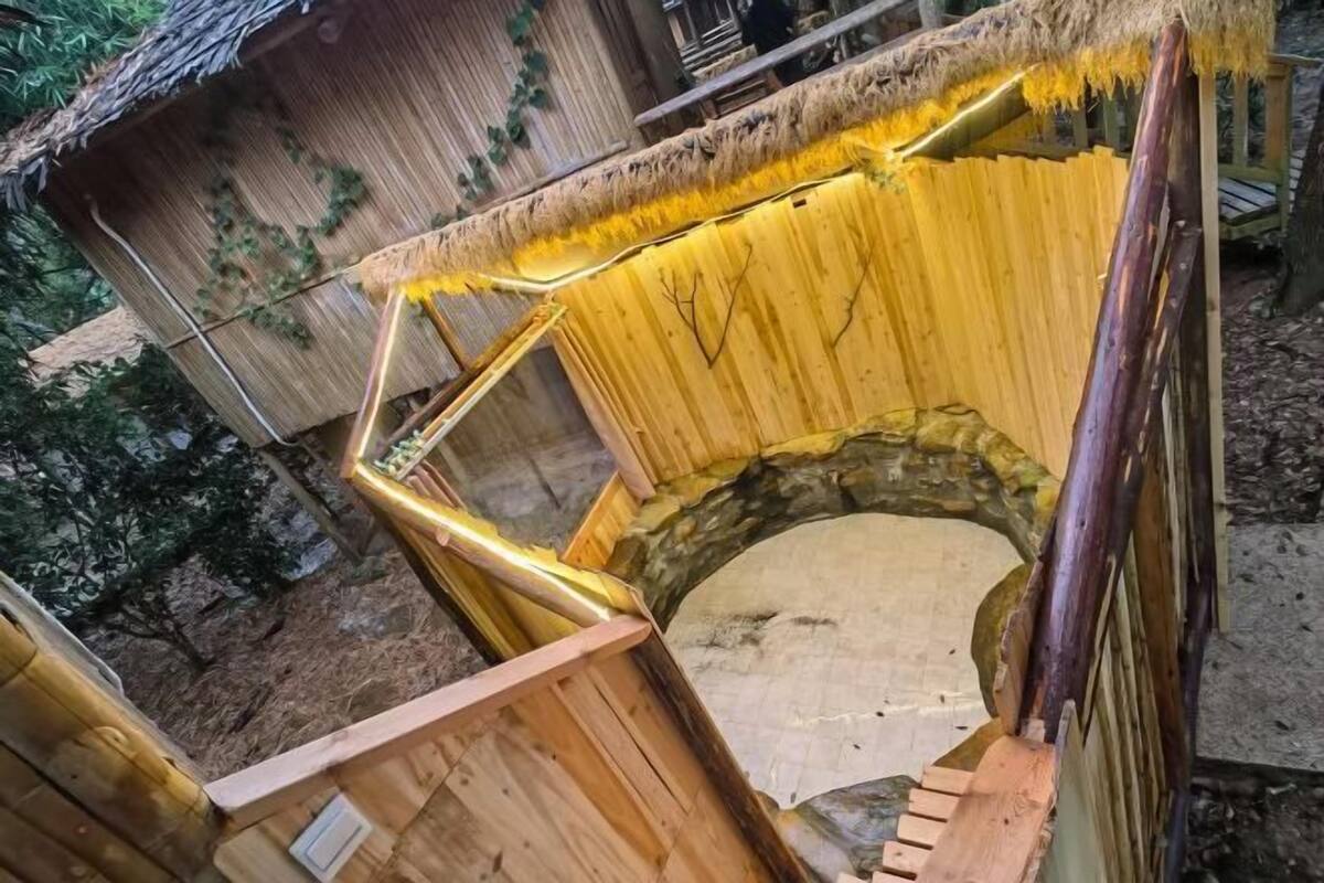 A wooden structure with a circular stone base, possibly a sauna or hot tub, surrounded by wooden walls and a thatched roof.