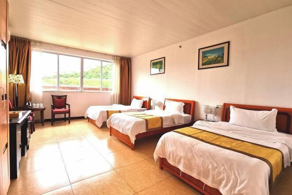 A hotel room with two single beds, a desk with a chair, a window with curtains, and two framed pictures on the wall.