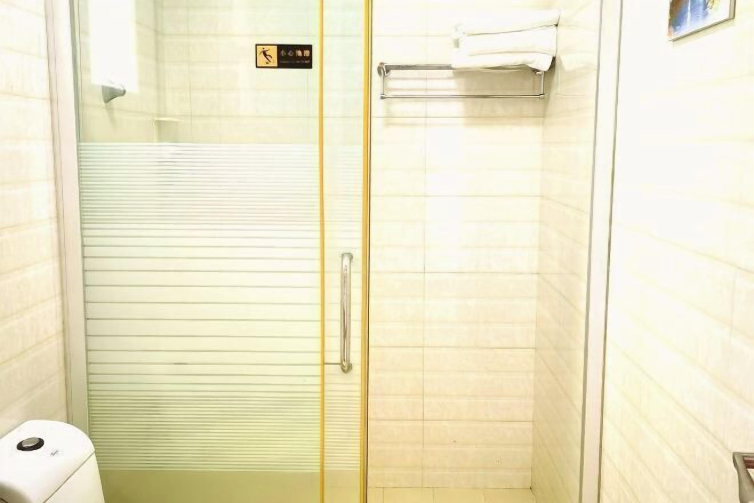 Un box de ducha con paredes de cristal, un inodoro y un perchero para toallas.
