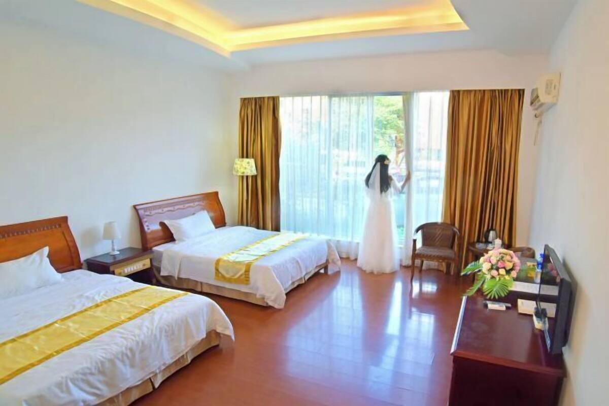 A hotel room with two beds, a desk, a chair, and a window with curtains.