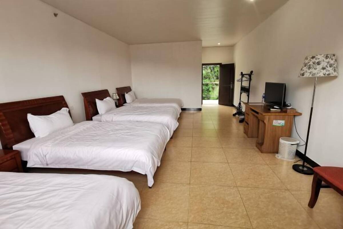 A hotel room with three beds, a desk with a computer, a TV, and a lamp.
