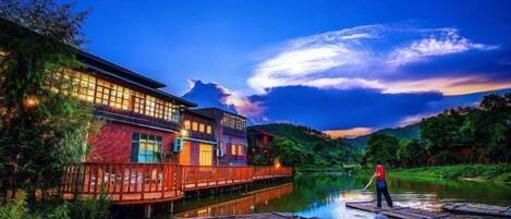 A riverside hotel with a wooden deck and a person standing on a boat.