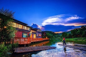 Hotel a orillas del río con una terraza de madera y una persona de pie en un bote.