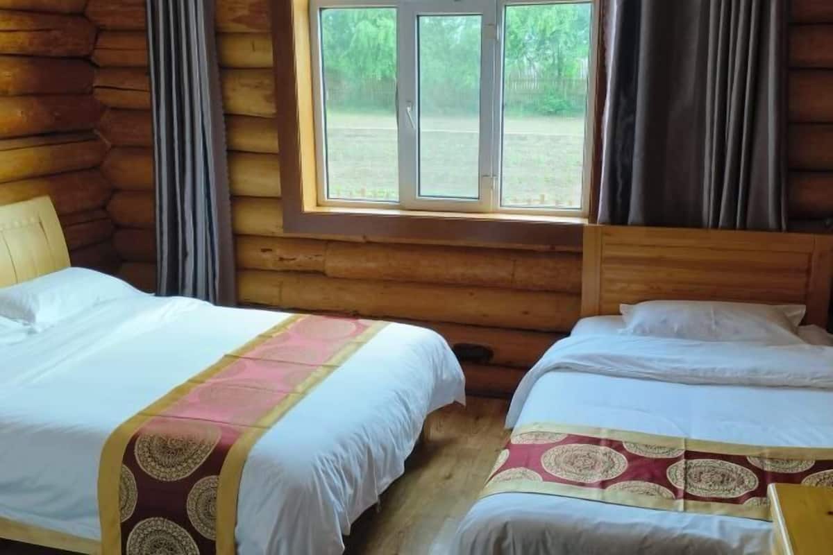 Una cabaña con dos camas, una ventana con cortinas y una pared de troncos.