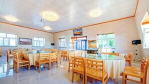 A spacious dining area with round tables and chairs, large windows, and a high ceiling. - Erguna Shiwei Radio & Tv Hotel (Ergun)