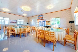 A spacious dining area with round tables and chairs, large windows, and a high ceiling. - Erguna Shiwei Radio & Tv Hotel (Ergun)