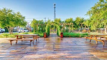 An outdoor wooden deck with picnic tables, surrounded by greenery and a clear sky.