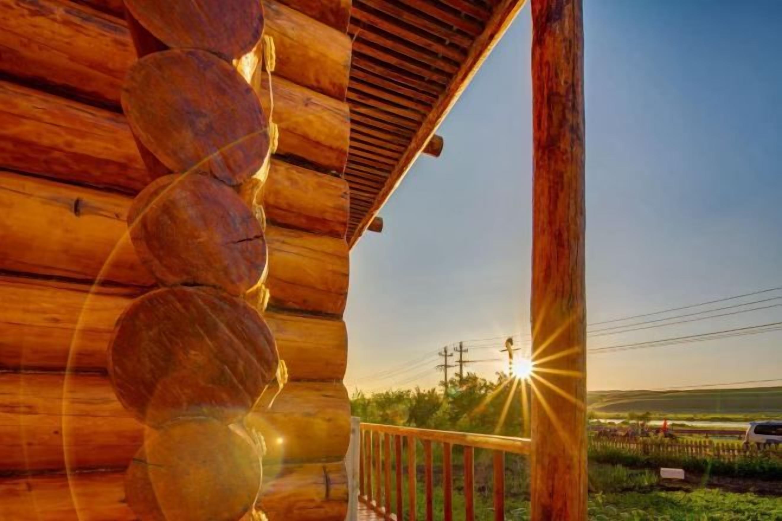 A wooden cabin with a spiral staircase, a wooden deck, and a view of the sunset over a field.