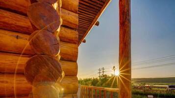 A wooden cabin with a spiral staircase, a wooden deck, and a view of the sunset over a field.