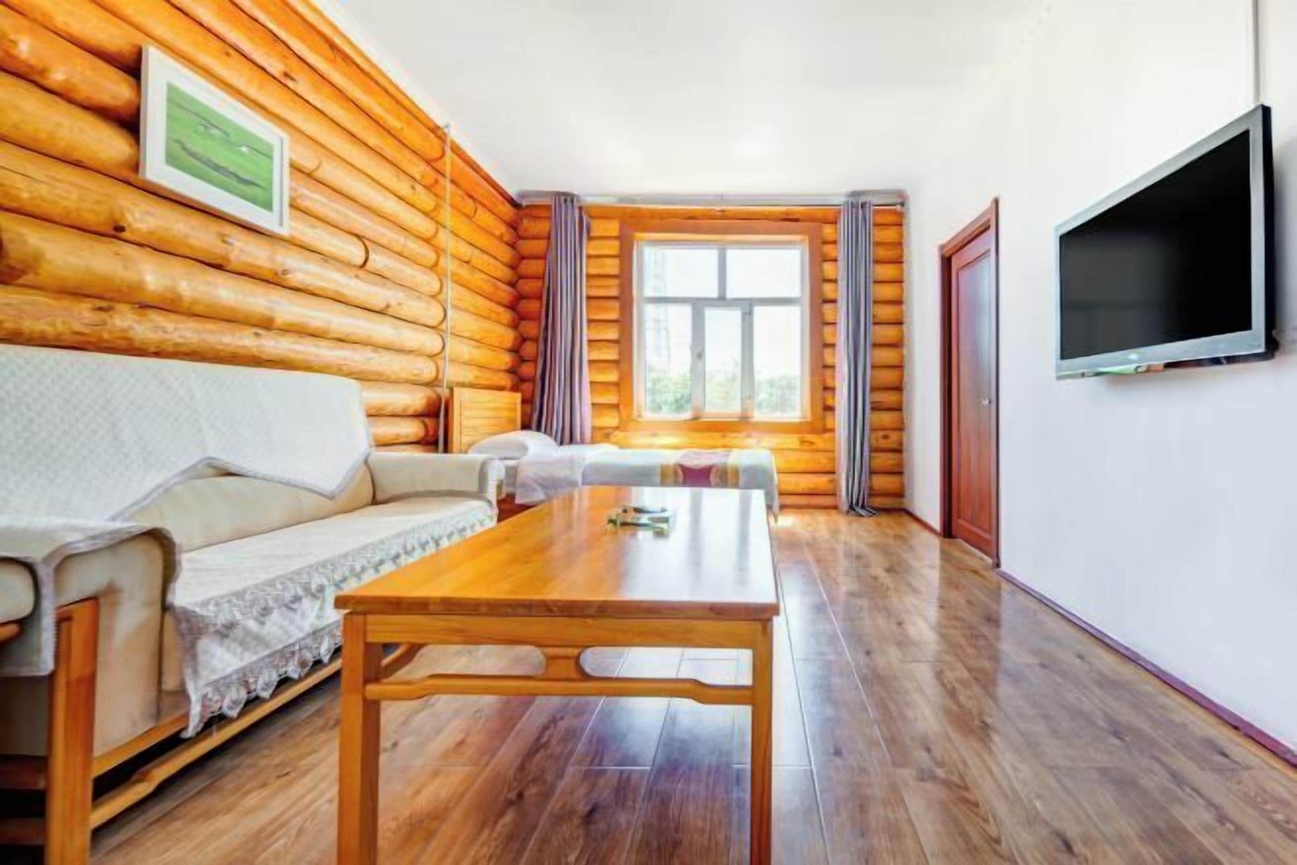 A log cabin room with a wooden floor, a sofa, a table, a TV, and a window with curtains.
