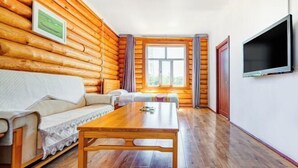 A log cabin room with a wooden floor, a sofa, a table, a TV, and a window with curtains. - Erguna Shiwei Radio & Tv Hotel (Ergun)