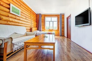 A log cabin room with a wooden floor, a sofa, a table, a TV, and a window with curtains. - Erguna Shiwei Radio & Tv Hotel (Ergun)