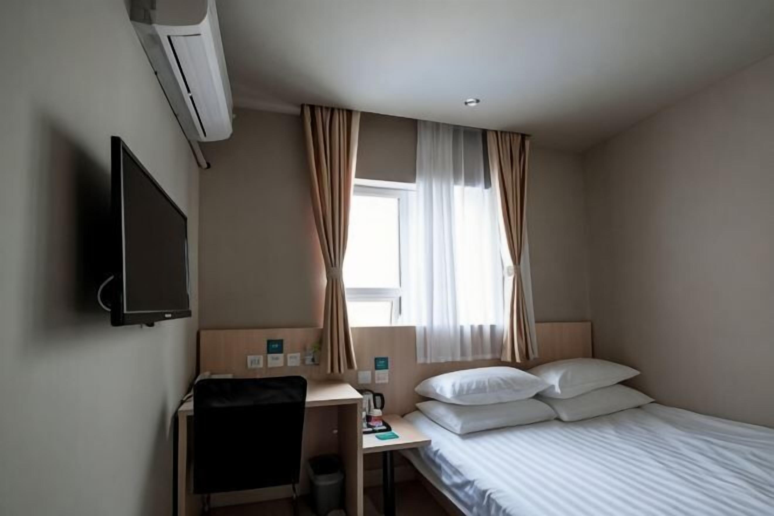 Hotellihuone, jossa on sänky, työpöytä, tuoli, televisio ja ikkuna, jossa on verhot.