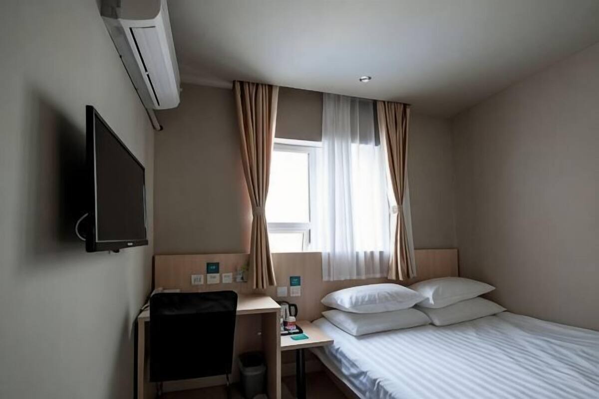 Una habitación de hotel con cama, escritorio, silla, televisor y ventana con cortinas.