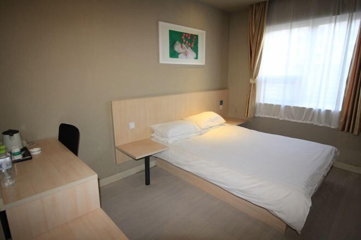 A hotel room with a bed, a desk, a chair, a picture on the wall, and a window with curtains.