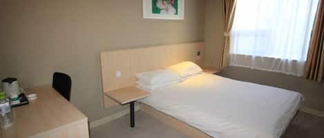A hotel room with a bed, a desk, a chair, a picture on the wall, and a window with curtains.