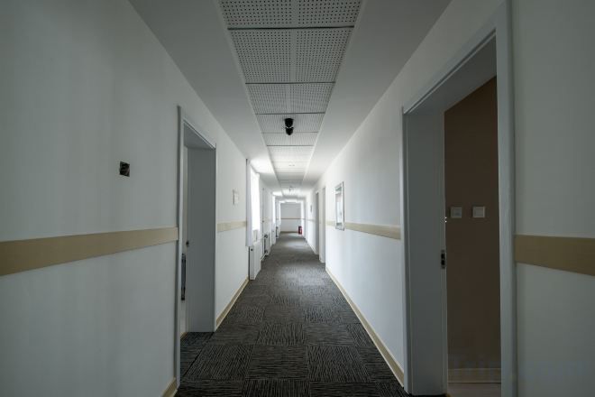 Ein langer, schmaler Hotelkorridor mit Türen an beiden Seiten, Teppichboden und einer Decke mit Gittermuster.