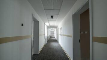 Ein langer, schmaler Hotelkorridor mit Türen an beiden Seiten, Teppichboden und einer Decke mit Gittermuster.
