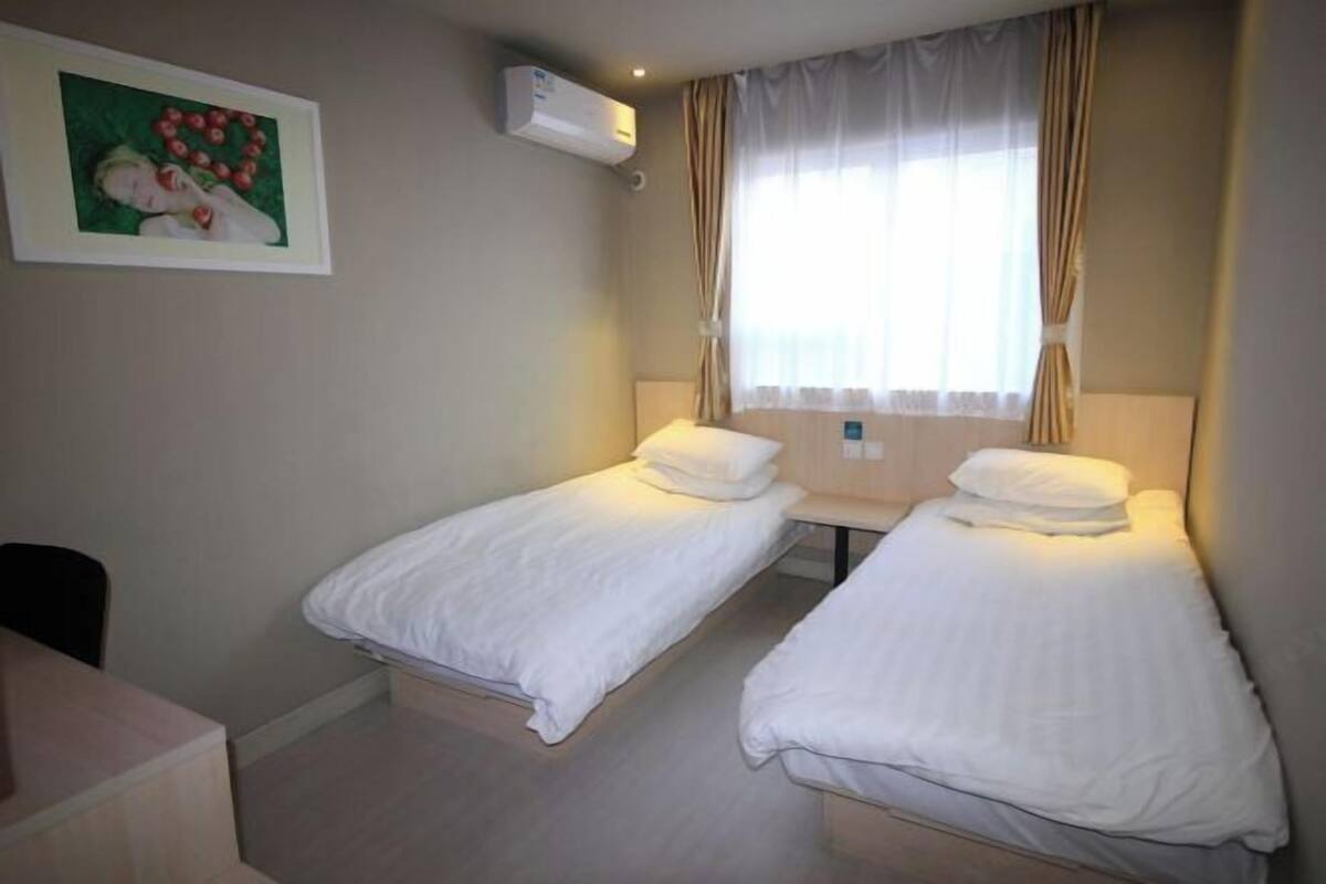 Habitación de hotel con dos camas individuales, un escritorio pequeño y una ventana con cortinas.