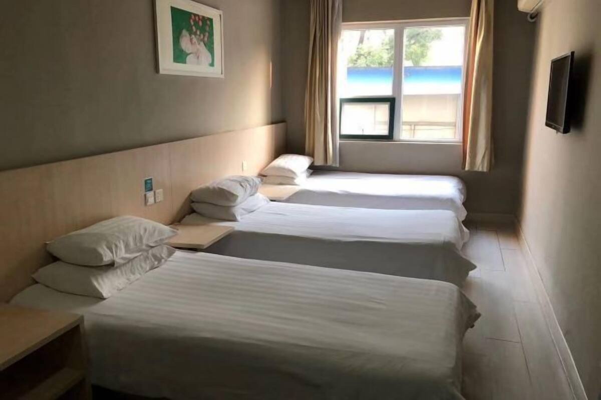 Habitación de hotel con tres camas individuales, una ventana con vista a la playa y un televisor de pantalla plana en la pared.