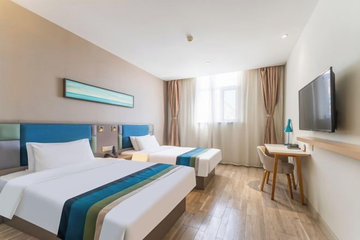 Una habitación de hotel con dos camas, un escritorio, un televisor y un cuadro en la pared.
