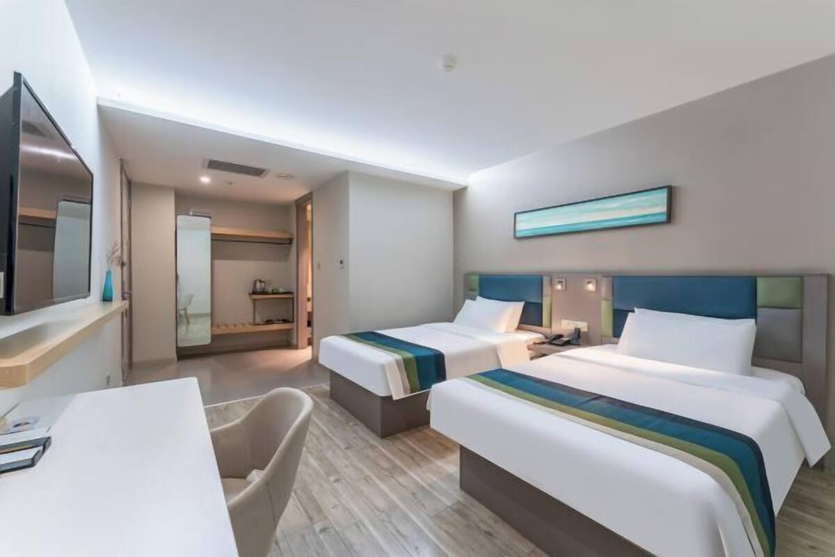 A hotel room with two beds, a desk, a chair, a TV, and a bathroom visible through an open door.