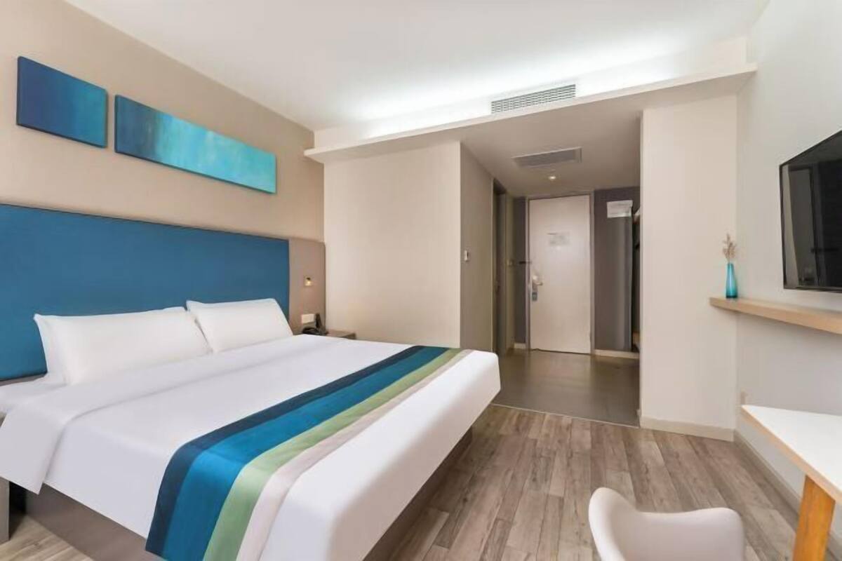A hotel room with a bed, a desk, and a television. There is a door leading to another room.