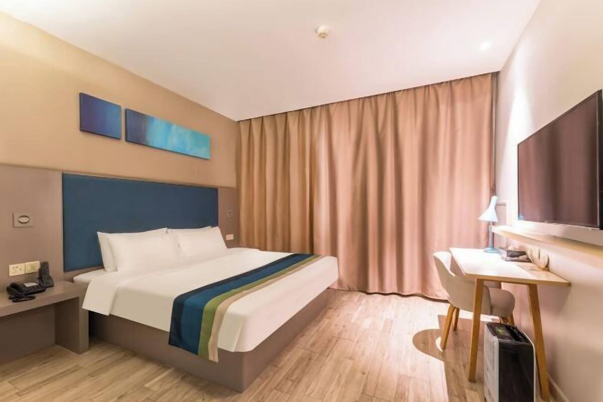 A hotel room with a bed, bedside table, desk, chair, and a television.