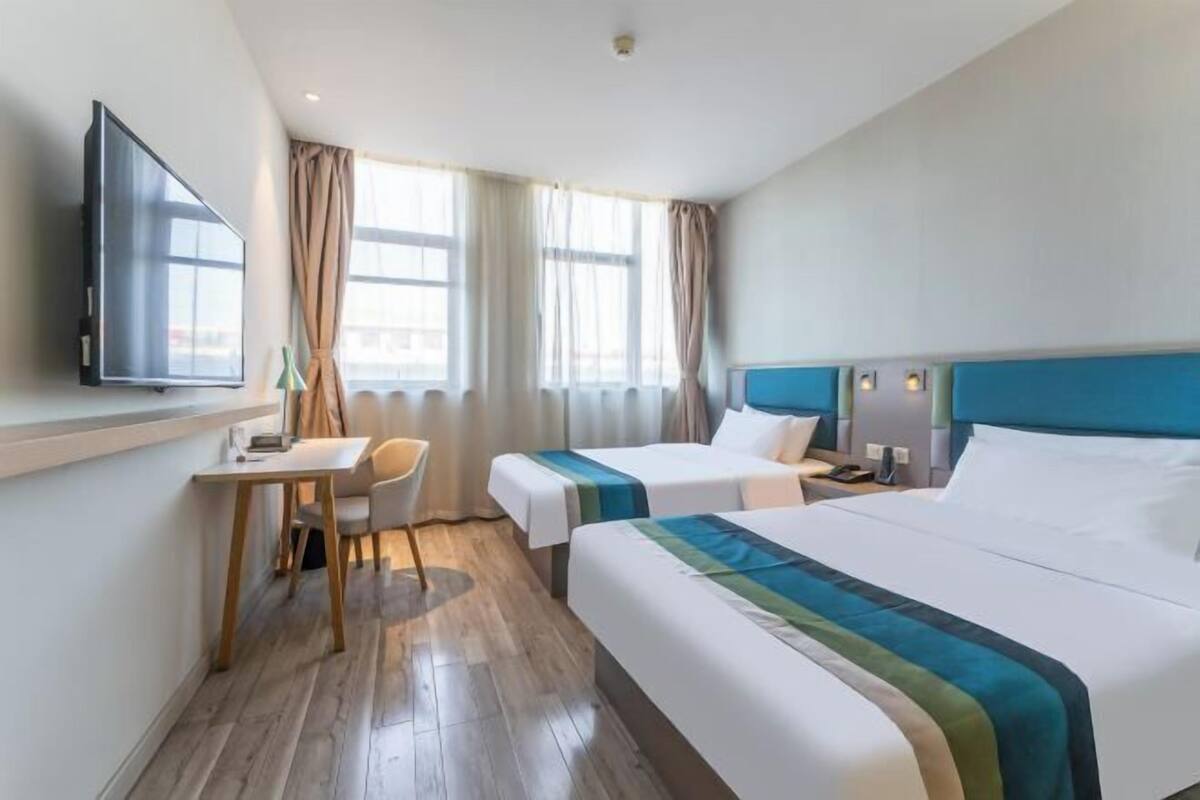 A hotel room with two beds, a desk, a chair, a television, and a window with curtains.