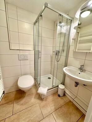 Ein Badezimmer mit Duschkabine, Toilette und Waschbecken mit Spiegel darüber.