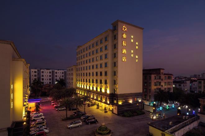 Ein mehrstöckiges Hotel mit gut beleuchteter Fassade, einem Parkplatz und einer begrünten Anlage mit Bäumen.