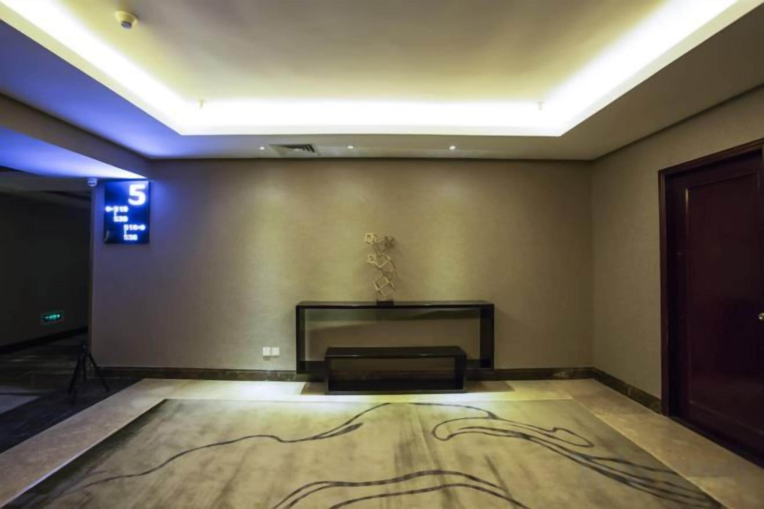A hotel lobby with a reception desk, a digital clock displaying the time, and a patterned carpet.