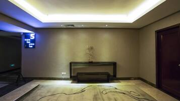 A hotel lobby with a reception desk, a digital clock displaying the time, and a patterned carpet.