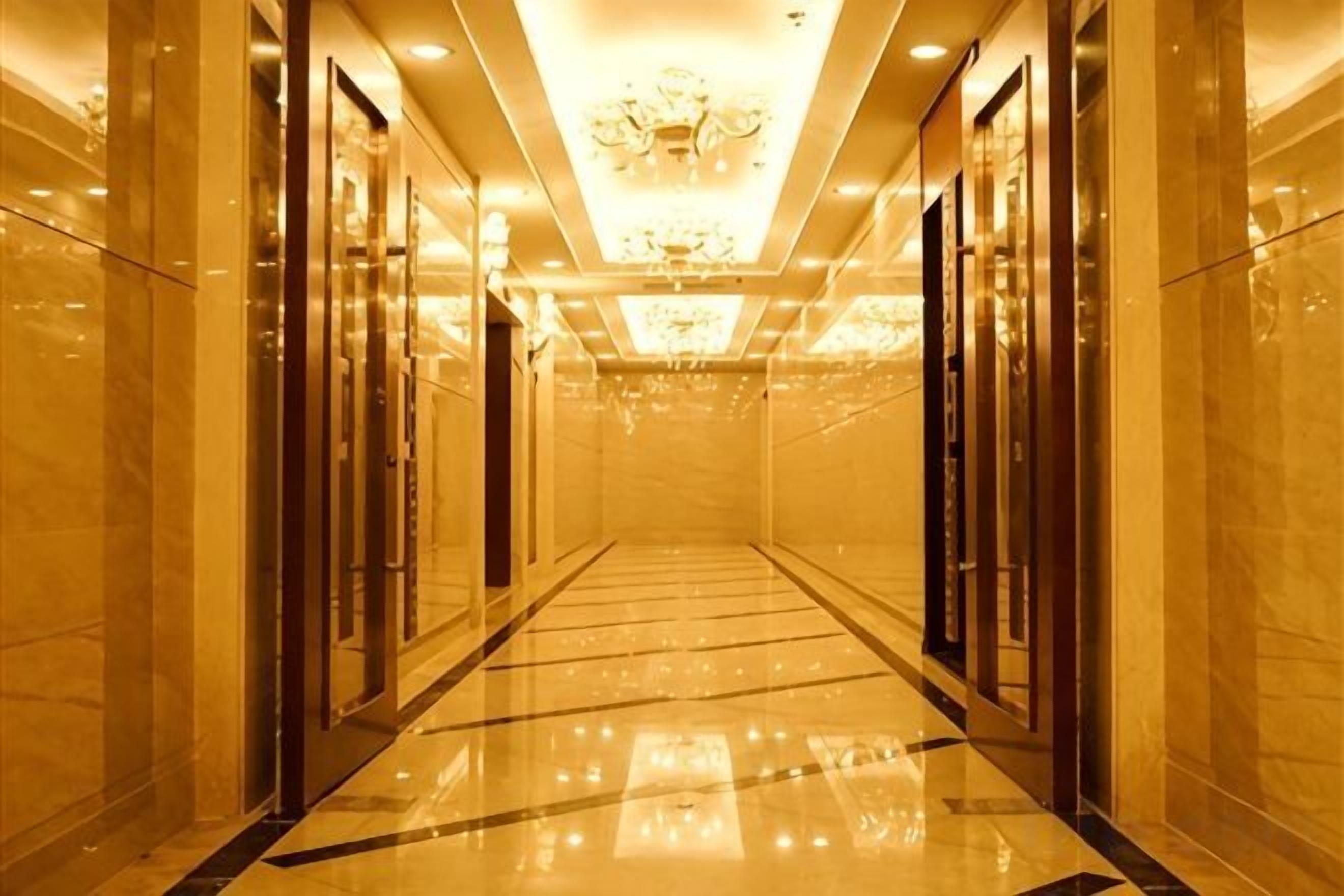 A long, narrow hallway with a reflective floor, doors on both sides, and a chandelier on the ceiling.