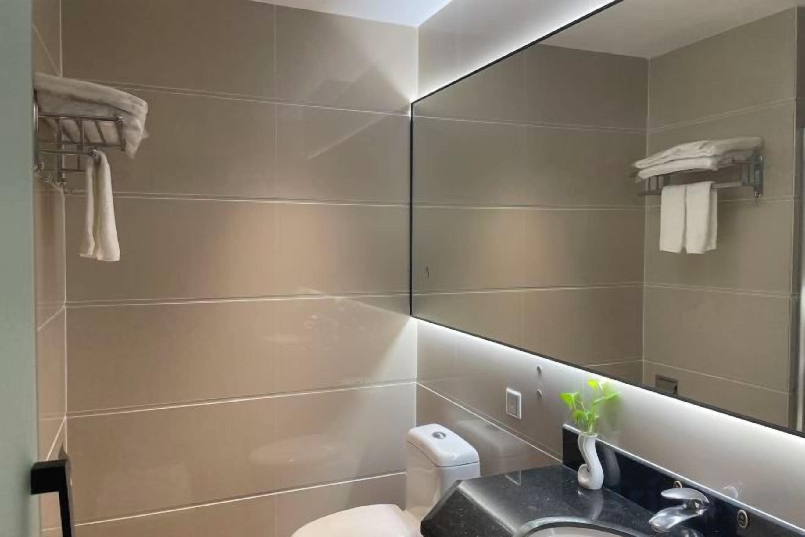Un baño moderno con un espejo grande, un inodoro y un lavamanos.