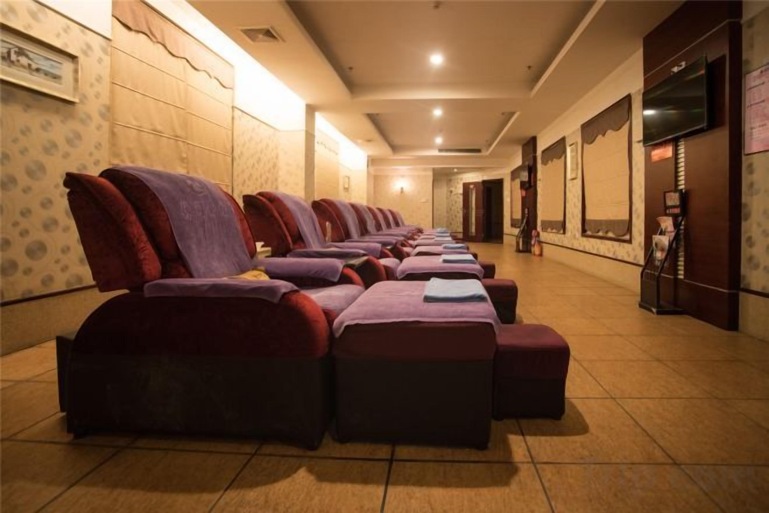 A row of massage chairs in a room with tiled flooring and a wall-mounted TV.