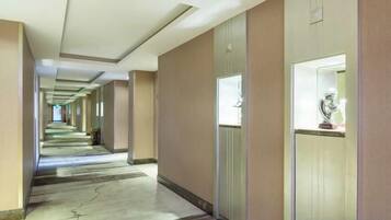 A long, narrow hotel corridor with doors on one side and a carpeted floor.